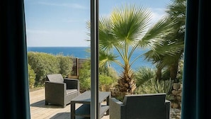 Un dormitorio con un amplio ventanal que da a un patio amueblado al aire libre, con mobiliario y una palmera.