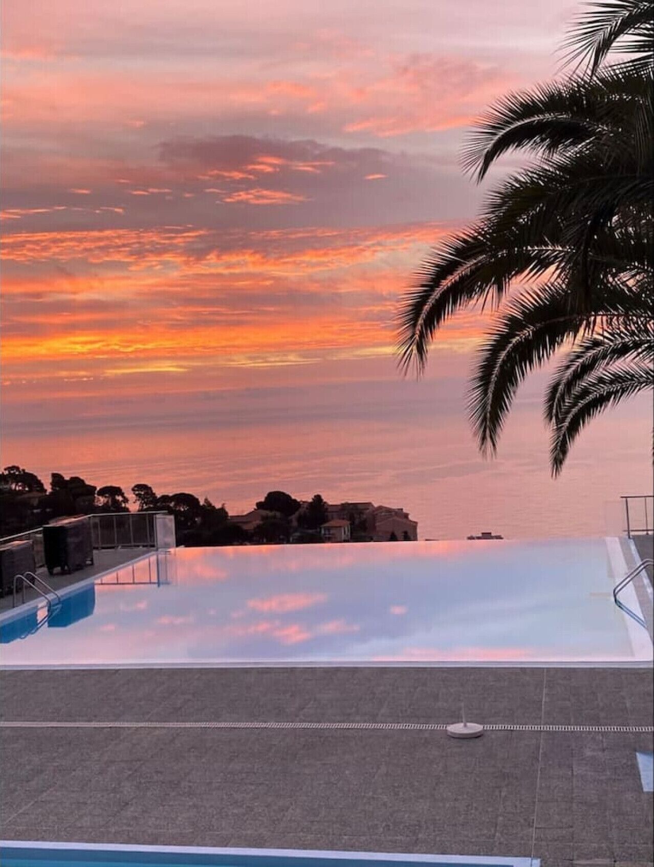 Une piscine à débordement offrant une vue sur le coucher de soleil au-dessus d’un quartier résidentiel.