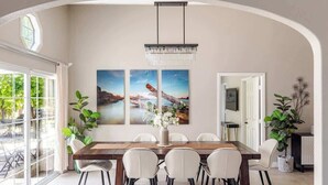 A dining area with a long table, six chairs, a chandelier, and three framed pictures on the wall. - Disneyland/Knott's 6BR, 4BA, 3000 sqft, No Tax (Anaheim)