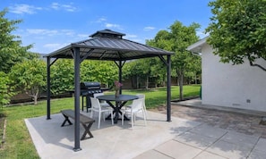 A covered patio with a grill, a round table, and chairs.
