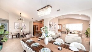A spacious living area with a dining table set for four, a kitchen in the background, and a modern chandelier. - Disneyland/Knott's 6BR, 4BA, 3000 sqft, No Tax (Anaheim)