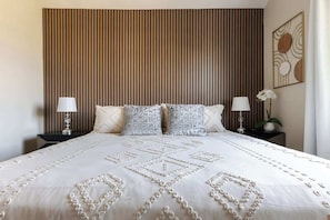 A bed with a patterned bedspread, two bedside lamps, and a wall-mounted artwork.