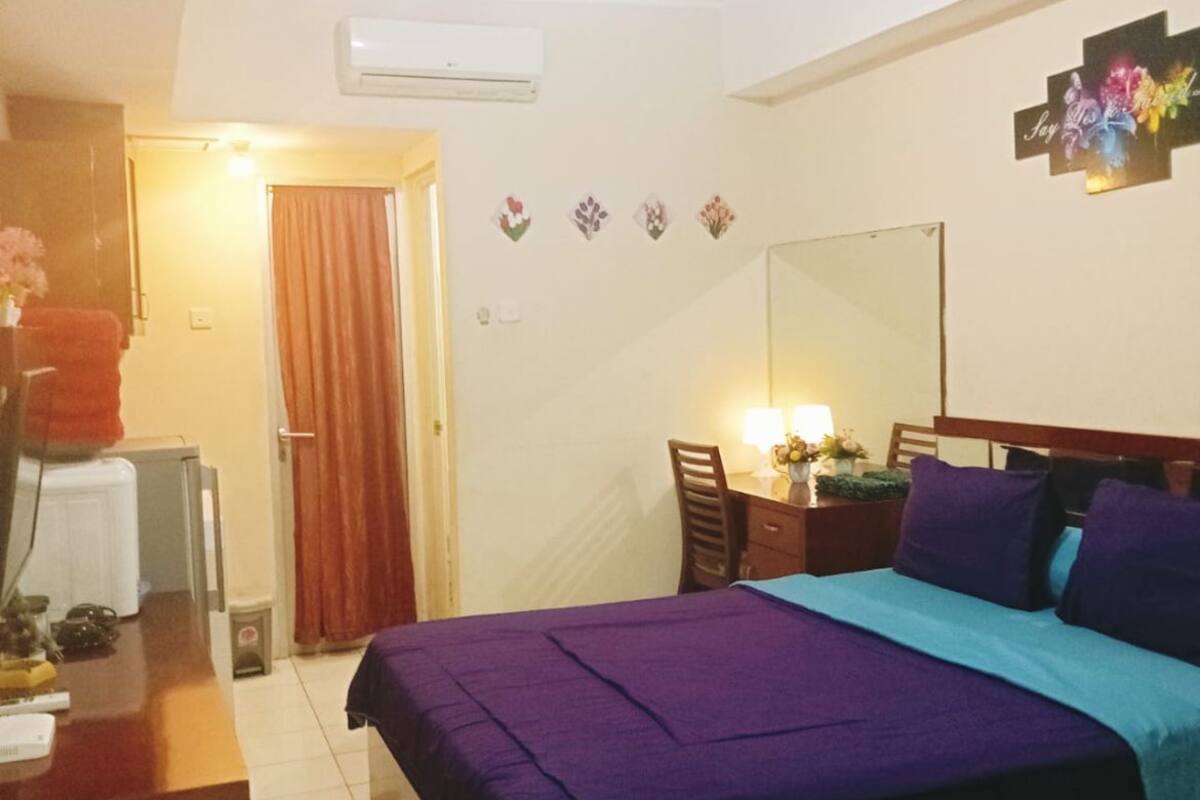 Een slaapkamer met een bed, bureau, stoel, spiegel en een airconditioner.