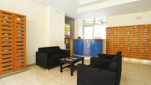 A reception area with black sofas, a coffee table, and orange storage units. - Capital O 93937 Aditya Rooms  (Depok)