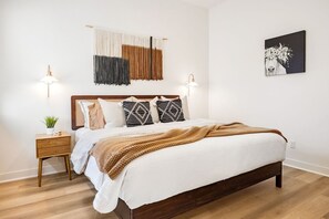 A bedroom with a wooden bed, two bedside lamps, a wall hanging, and a framed picture. - Golf Lover's Haven: EV Charger, Private Pool & Spa (La Quinta)