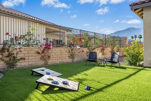 A backyard with artificial grass, two wooden tables, and chairs. - Golf Lover's Haven: EV Charger, Private Pool & Spa (La Quinta)