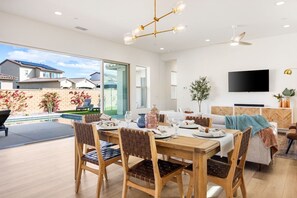 A modern dining area with a wooden table and chairs, a flat-screen TV mounted on the wall, and a view of the backyard.