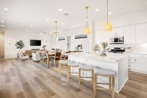 A modern kitchen with white cabinetry, a central island, and hanging pendant lights. - Golf Lover's Haven: EV Charger, Private Pool & Spa (La Quinta)