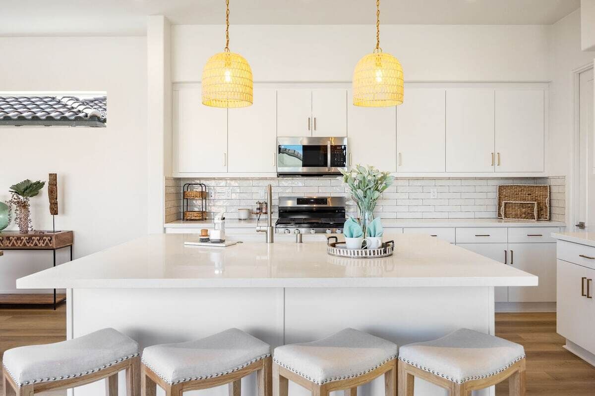 Een moderne keuken met witte kasten, een centraal eiland met barstoelen en hanglampen.