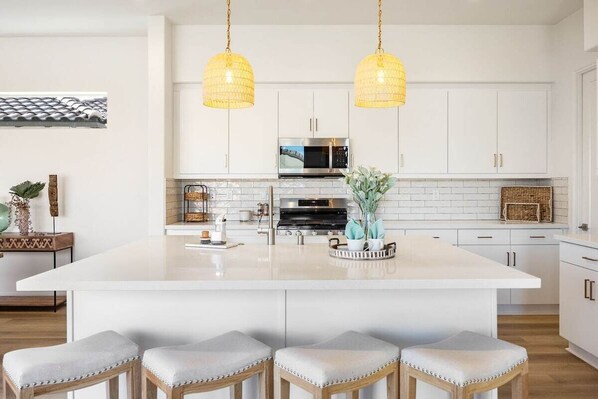 A modern kitchen with white cabinetry, a central island with bar stools, and pendant lighting.