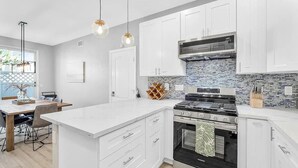 Una cucina moderna con mobili bianchi, piano cottura nero e schienale piastrellato.