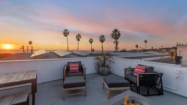 Una terrazza panoramica con poltrone relax, un braciere e vista su palme e tramonto.