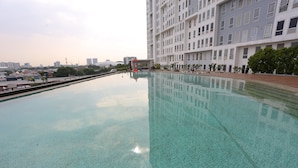 A large, clear swimming pool with a tiled surface, surrounded by a building with multiple windows and balconies. - Collection O 93914 Iconic Residence  (Bekasi)