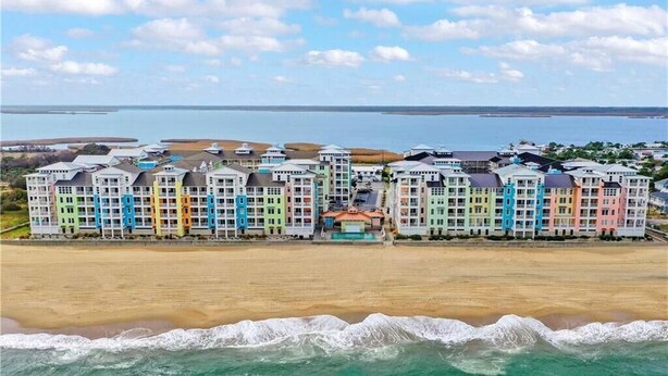 A beachfront hotel with colorful buildings, a pool, and a view of the ocean and distant land. - Book Lazy Waves 414B | Sandbridge Vacation Condo (Virginia Beach)