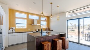 Une cuisine moderne dotée d’un grand îlot central, de luminaires suspendus et offrant une vue sur le paysage désertique.