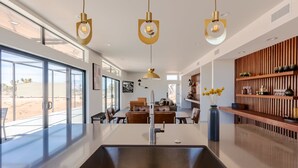 Une cuisine moderne dotée d’un îlot central, de luminaires suspendus et offrant une vue sur l’extérieur.