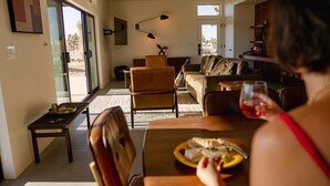 Un salon avec un canapé, des fauteuils, une table à manger sur laquelle se trouve une assiette de nourriture et un verre à vin.