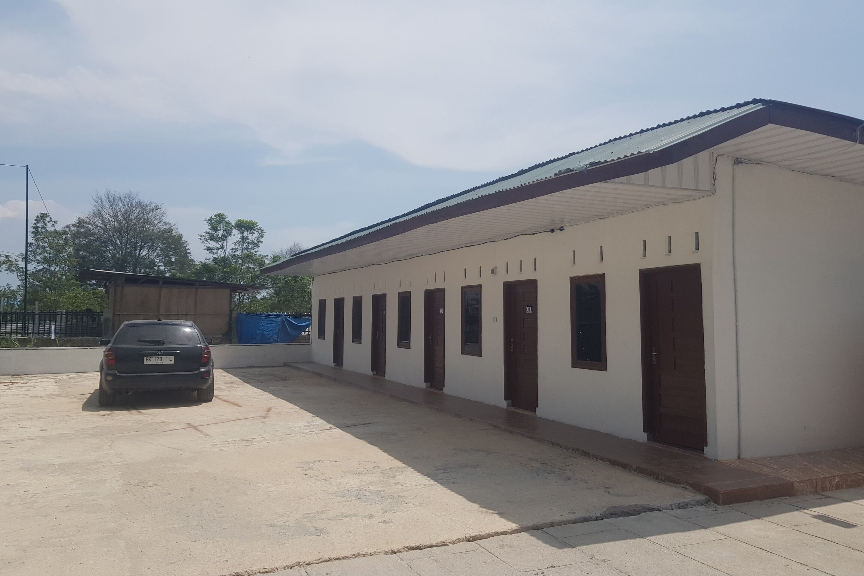 A building with a row of rooms, a covered parking area, and a car parked in front.