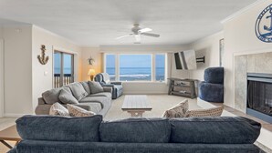 Een woonkamer met uitzicht op zee, een plafondventilator, een open haard en een televisie.
