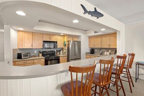 A modern kitchen with wooden cabinets, stainless steel appliances, and a curved island with bar stools.