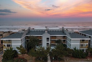 A multi-story hotel with a central courtyard, located near a beach with a view of the ocean.