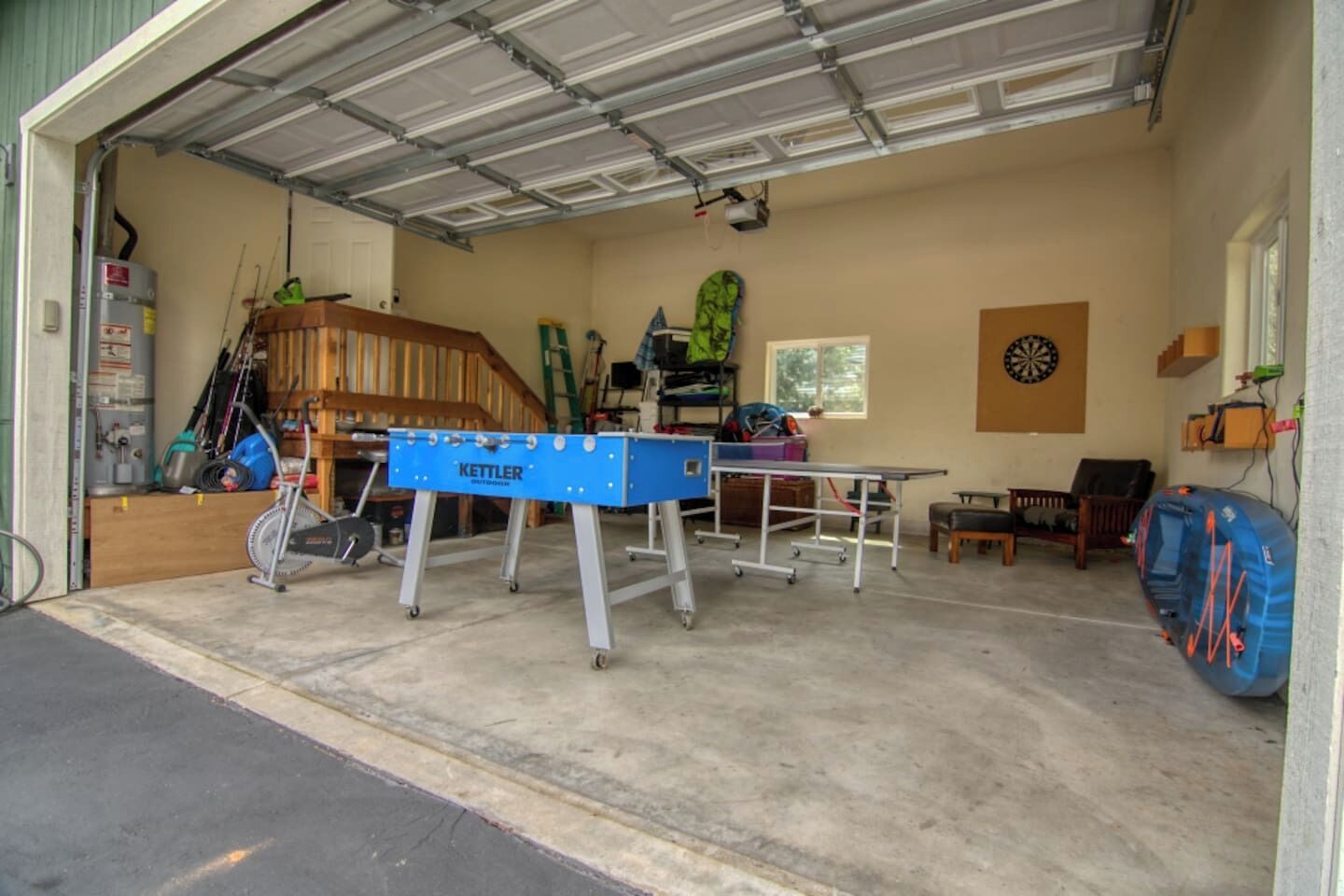 A garage with a foosball table, a dartboard, and various sports equipment.