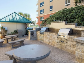 An outdoor patio with stone tables and a barbecue grill. - Jade East Towers #650 | Gulf Front, Resort Pool + Near Popular Attractions! (Destin)