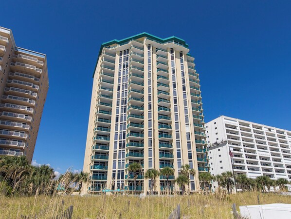 A high-rise hotel with multiple balconies, a flat roof, and a clear blue sky.