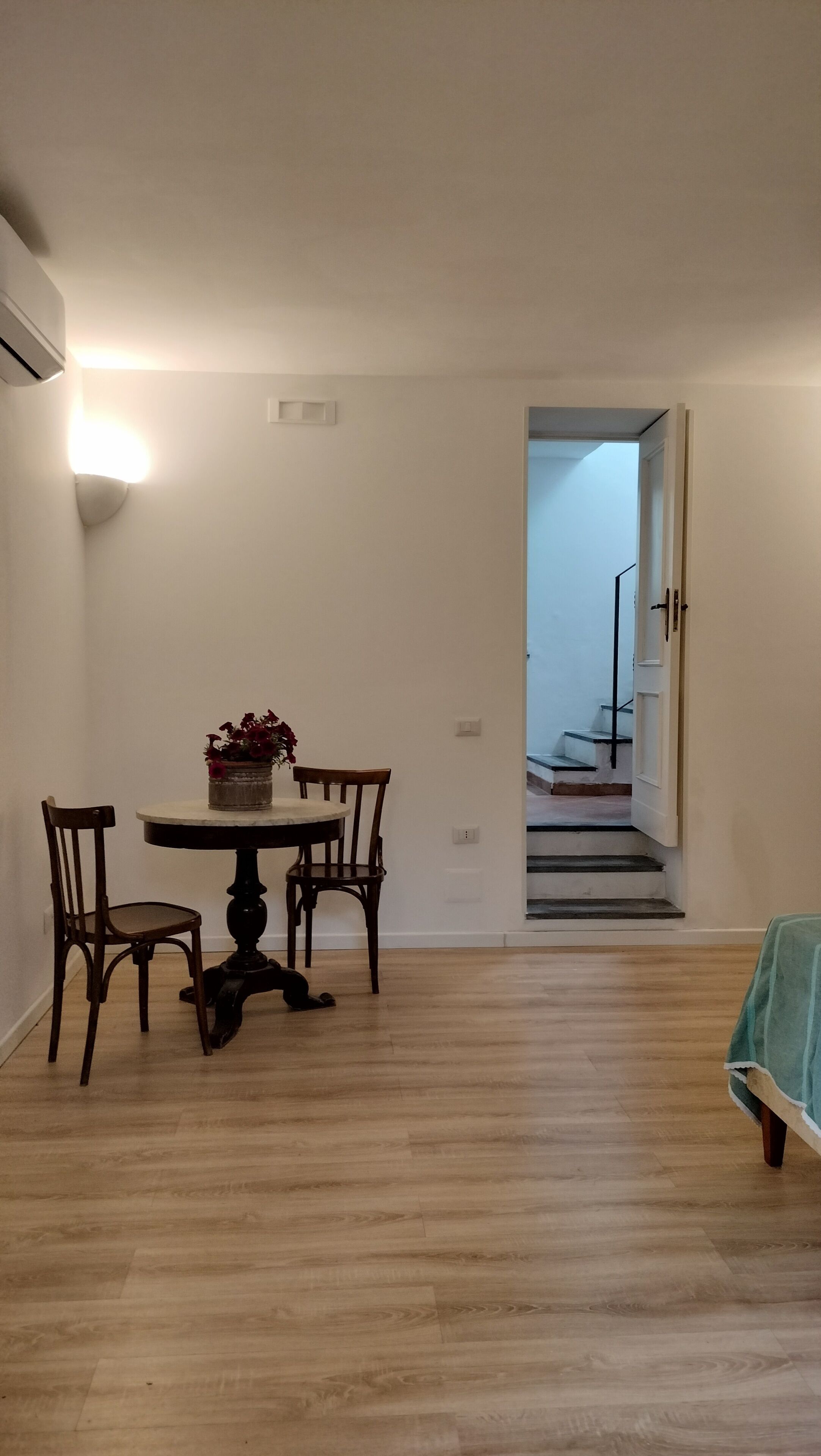 A dining area with a round table, two chairs, and a potted plant. A staircase is visible in the background leading to an upper floor.
