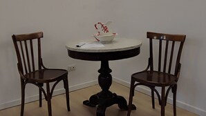A small dining area with a round table and two wooden chairs, a white wall, and a ceiling light. - Camera immersa nel verde (Sorrento)