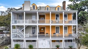 A two-story building with a balcony on each floor, a staircase on the left, and a small porch area with potted plants.