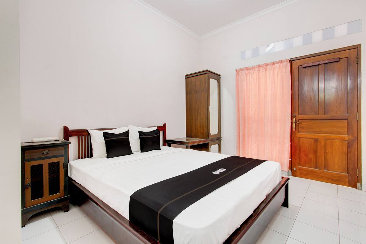 A neatly made bed with a black and white bedspread, a wooden nightstand with a mirror, and a wooden wardrobe.