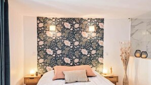A hotel room with a floral wallpaper, a bed with white linens, two bedside tables with lamps, and a vase with dried flowers. - ELEGANCE in the heart of the old town 4 **** (Annecy)