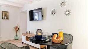 A modern dining area with a round table, two chairs, a flat-screen TV mounted on the wall, and decorative wall art. - ELEGANCE in the heart of the old town 4 **** (Annecy)