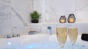 A bathtub with two glasses of champagne, a potted plant, and two candle holders on a marble-tiled wall. - ELEGANCE in the heart of the old town 4 **** (Annecy)