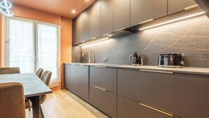 A modern kitchen with dark cabinets, a marble backsplash, and a built-in toaster. - L'OASIS T3 Centre ville (Annecy)