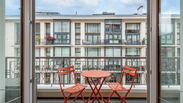 A balcony with two red chairs and a small table, overlooking a multi-story building with balconies and windows. - L'OASIS T3 Centre ville (Annecy)
