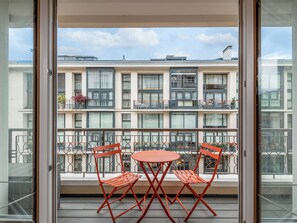 Un balcón con dos sillas rojas y una mesita, con vistas a un edificio de varios pisos con balcones y ventanas.