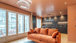 A modern living room with a sofa, a round table, and a kitchen area with dark cabinets and a marble backsplash. - L'OASIS T3 Centre ville (Annecy)