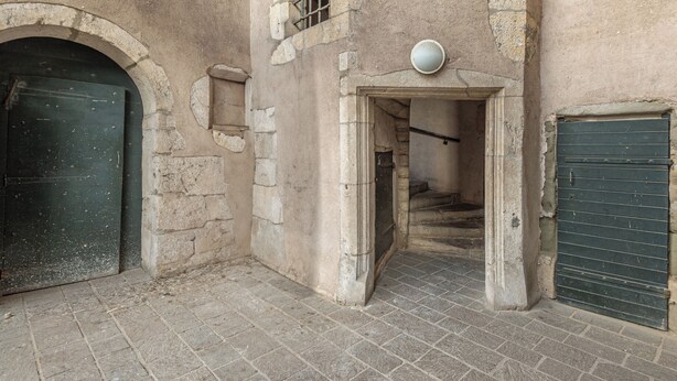 Un patio interior con paredes de piedra, una puerta verde y una ventana pequeña con barrotes.