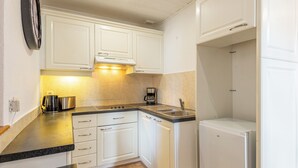 Una cocina compacta con armarios blancos, una encimera negra, cafetera y refrigerador.