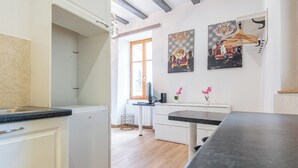 Cocina moderna con armarios blancos, encimera negra y suelo de madera. Se observan dos cuadros en la pared, una ventana y un radiador.