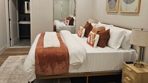 A modern bedroom with a large bed, a bedside table with a lamp, and a mirror above the bed.