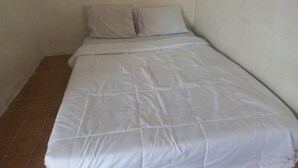 A small, single-bed room with a plain white bedspread and two pillows. The room has plain walls and a tiled floor. - Hotel O Homestay Adreena Syariah (Purwokerto)