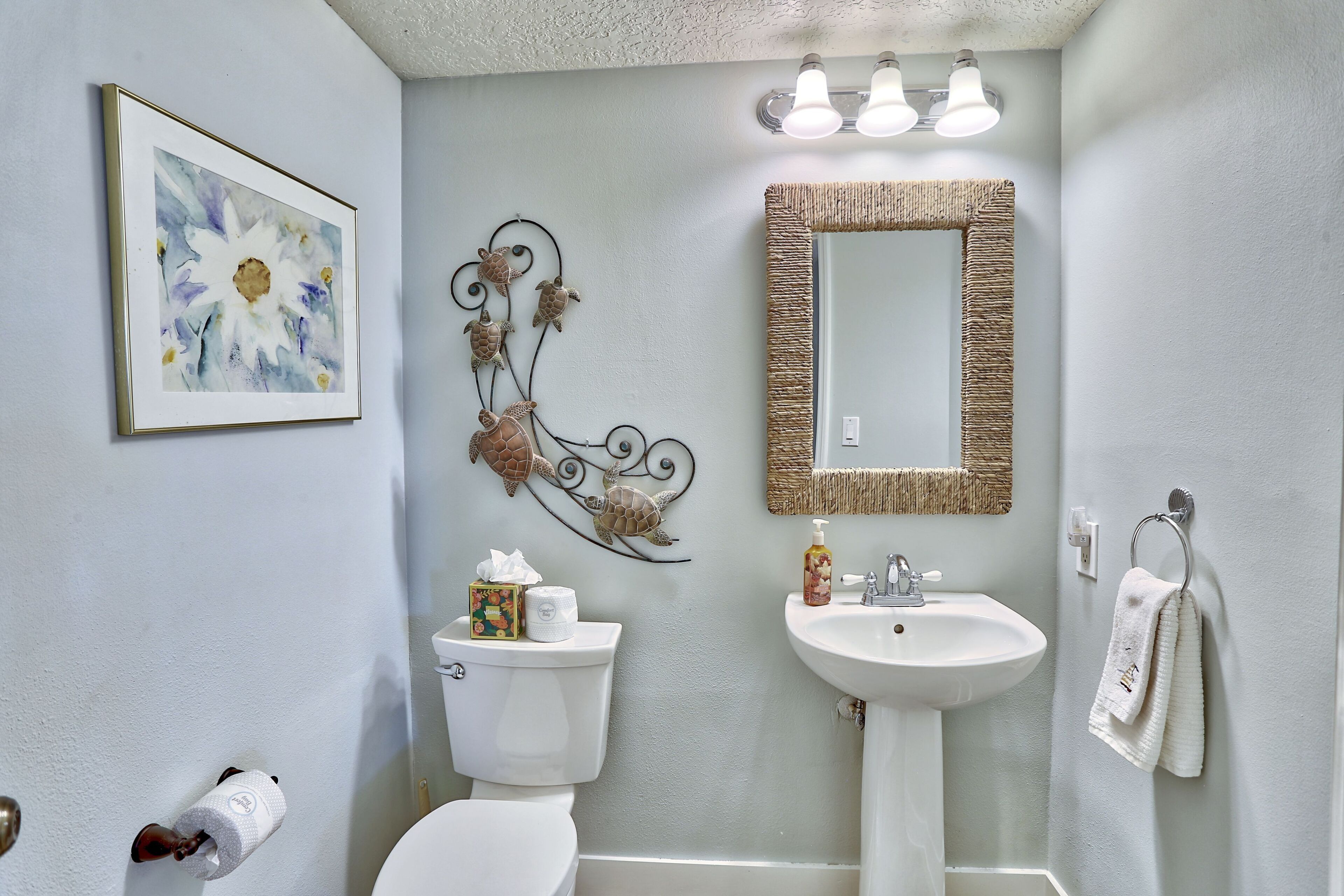 A bathroom with a toilet, sink, and mirror. There is a framed artwork on the wall and a towel rack with towels.