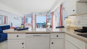 Une cuisine moderne avec un îlot central, un coin repas offrant une belle vue et un salon doté d’un canapé bleu.
