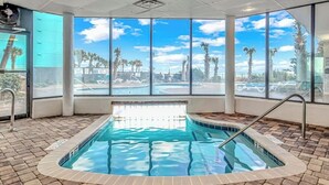 Un espace piscine avec une eau d’un bleu limpide, une terrasse carrelée et de grandes fenêtres offrant une vue sur les palmiers et un ciel dégagé.