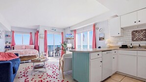 Une chambre d’hôtel moderne dotée d’un balcon, d’une cuisine et d’un espace de vie comprenant un canapé et une table basse.