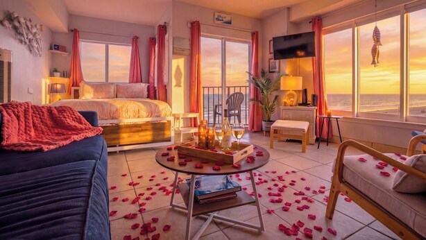 Une chambre d’hôtel avec un lit, un canapé, une petite table avec des boissons, une télévision et un balcon avec vue.
