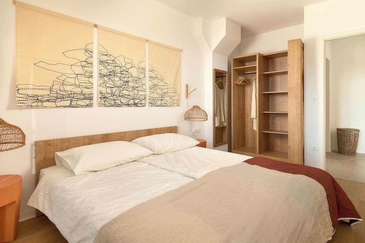 A bedroom with a bed, a wooden wardrobe, and a large abstract painting on the wall.